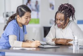 A senor patient of African decent, sits across the desk from her female doctor as they go over her recent lab results on a tablet in front of them.  The woman is dressed casually and leaning in closely to look at the screen as the doctor explains what she is seeing.